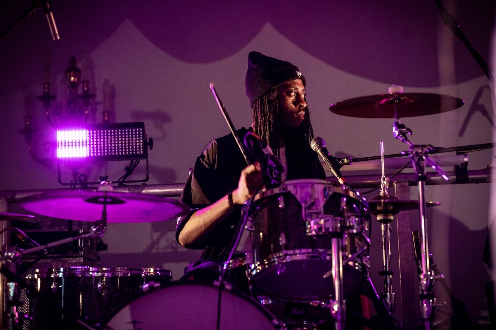 Jagun playing a live drum set under purple stage lights